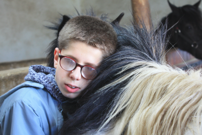 jeune garçon handicapé posant sa tête contre l'encolure d'un poney