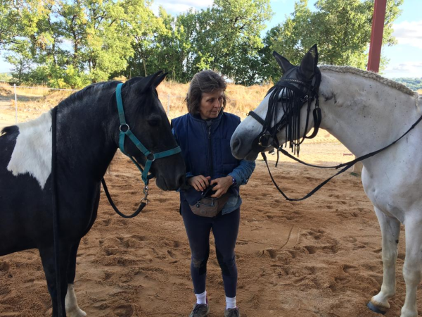Marie-Noëlle Gachet entourée par deux chevaux ; elle leur parle et ils écoutent attentivement.