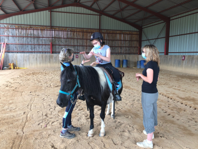 un jeune cavalier handicapé récompense son cheval à l'arrêt dans le manège, sous l'oeil de marie-noëlle gachet et d'une éducatrice