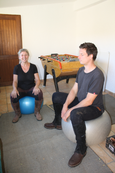 Deux adultes font des exercices de positionnement en étant assis sur de gros ballons ; ils ont les yeux fermés et se relaxent.