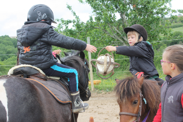 Deux enfants face à face sur leurs poneys, se transmettent un témoin en apprenant à maîtriser leur monture.