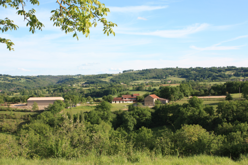 Vue lointaine de la ferme équestre de Saint-Gauzy (Aveyron - Occitanie), avec les prés alentours.